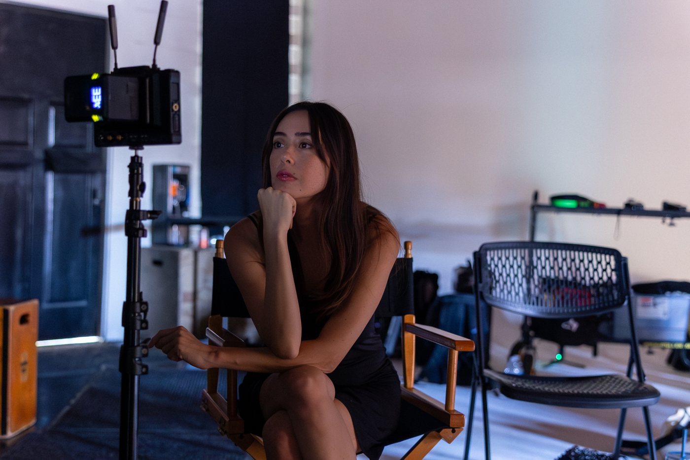 Kat Mills Martin in a director’s chair on set, chin resting on her hand